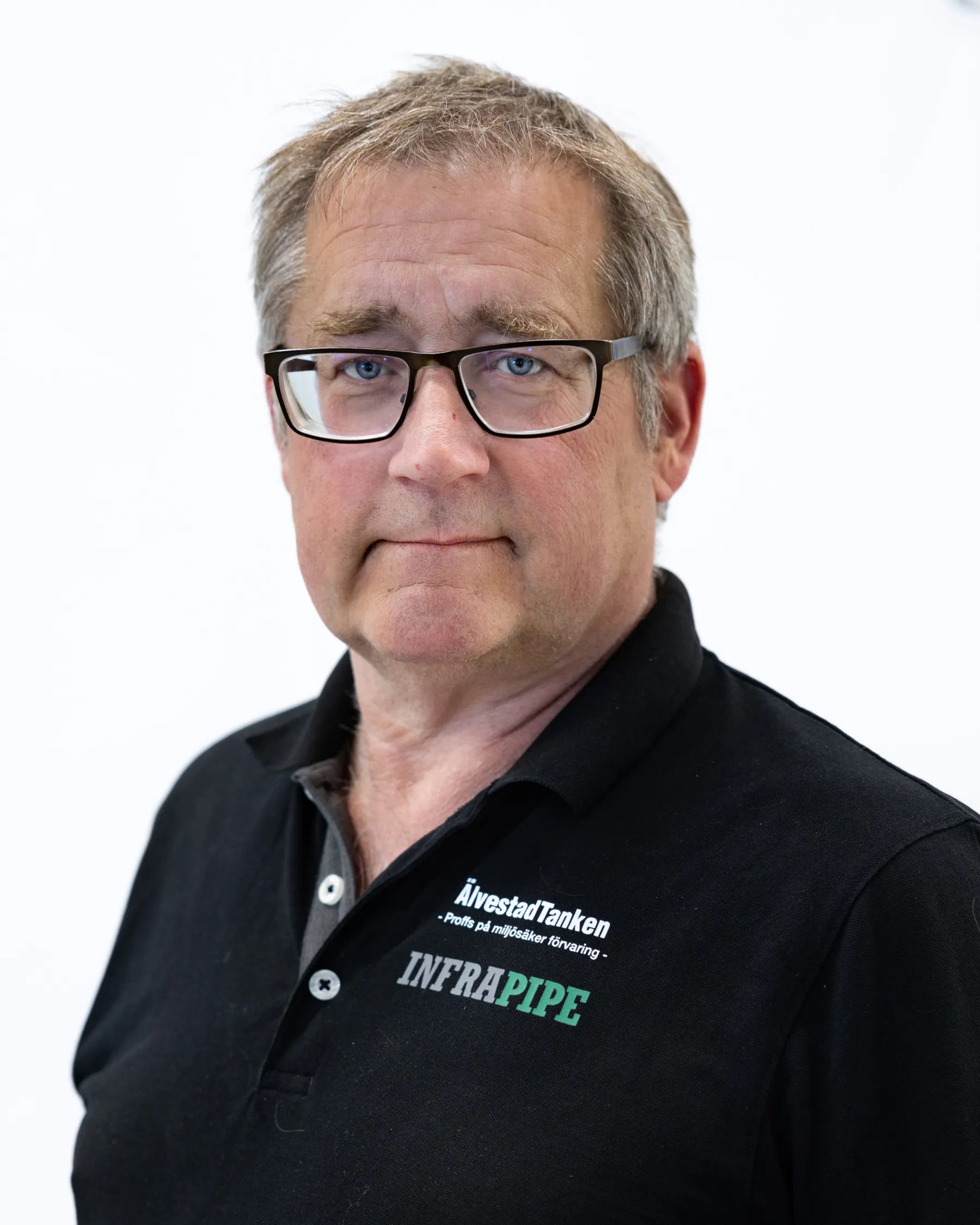 En medelålders man med kort grått hår och glasögon, klädd i en svart polotröja med INFRAPIPE och annan text, står mot en vit bakgrund.