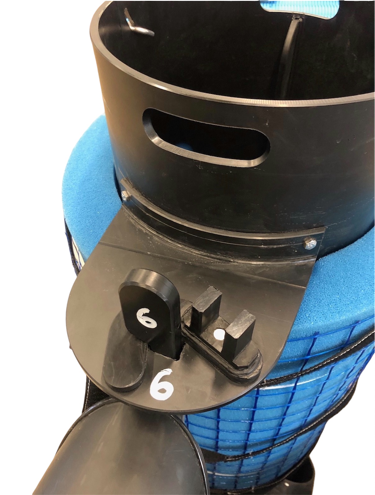 Närbild av en svart plastdel märkt "6" i vitt, fäst vid blått skum och nät på Oljeavskiljare betong ESK-H 3/600, med slitsar och handtag - troligen använd vid filtrering eller rengöring.