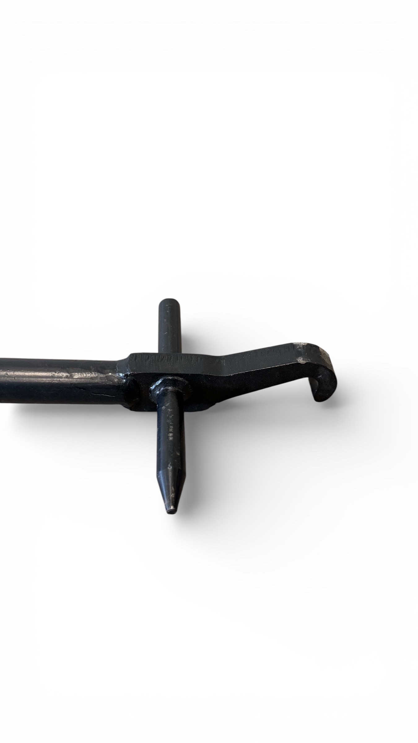 Närbild av Öppningsverktyg till betäckning, ett verktyg i svart metall med spetsig spets, centralt skaft och krokig ände, mot vit bakgrund.