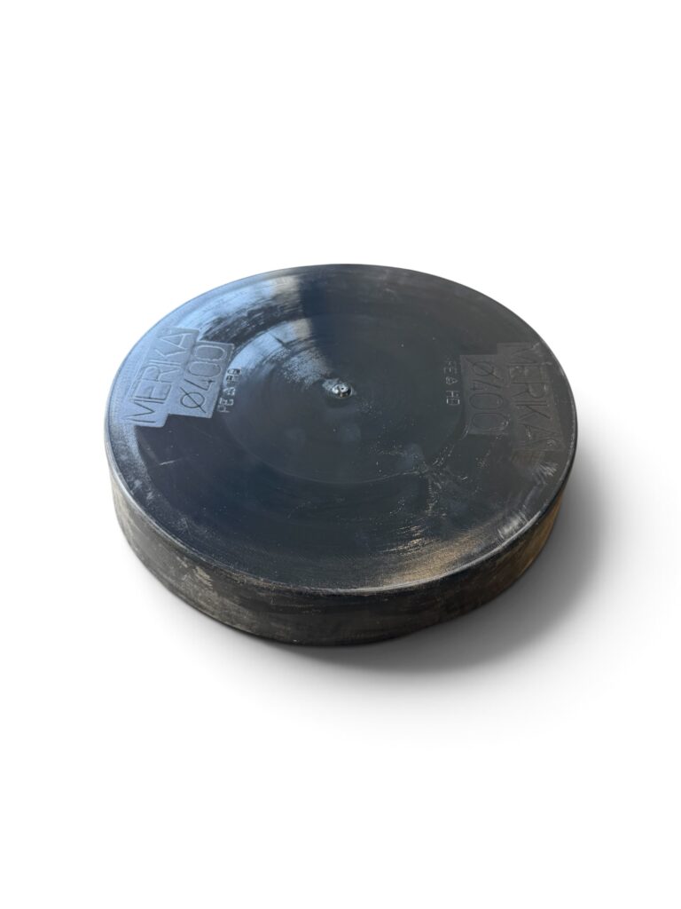 En svart, rund puck av massivt gummi med präglad text på ytan – märkt ”Plastlock 400 mm till PP-stigarrör” – är placerad på en vit bakgrund med en svag skugga under.