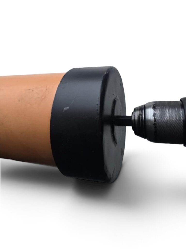 En närbild av ett Rörfas 110 mm markeringsrör monterat på en borrmaskin, med ett svart runt lock i änden av det bruna cylindriska föremålet, fotograferat mot en vit bakgrund.